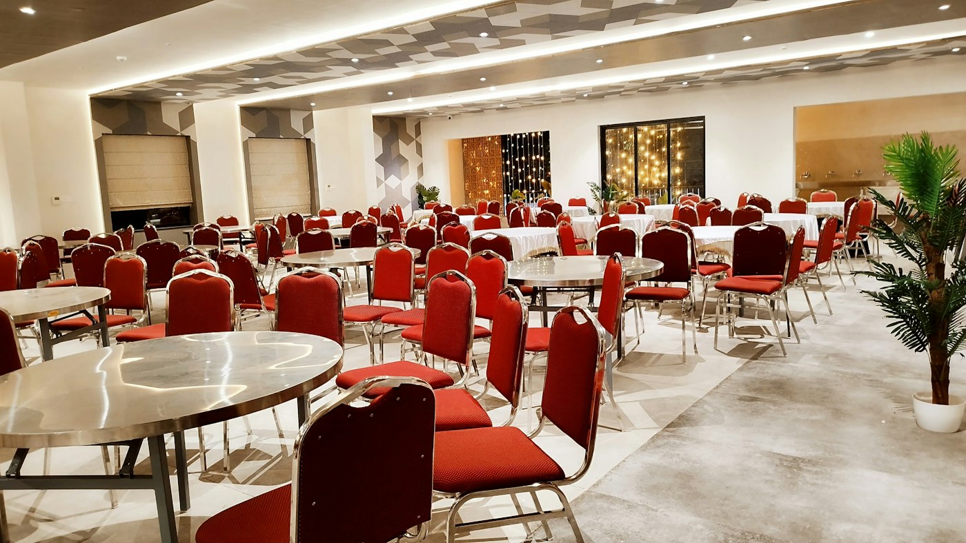 An empty banquet room set with round tables and red chairs.