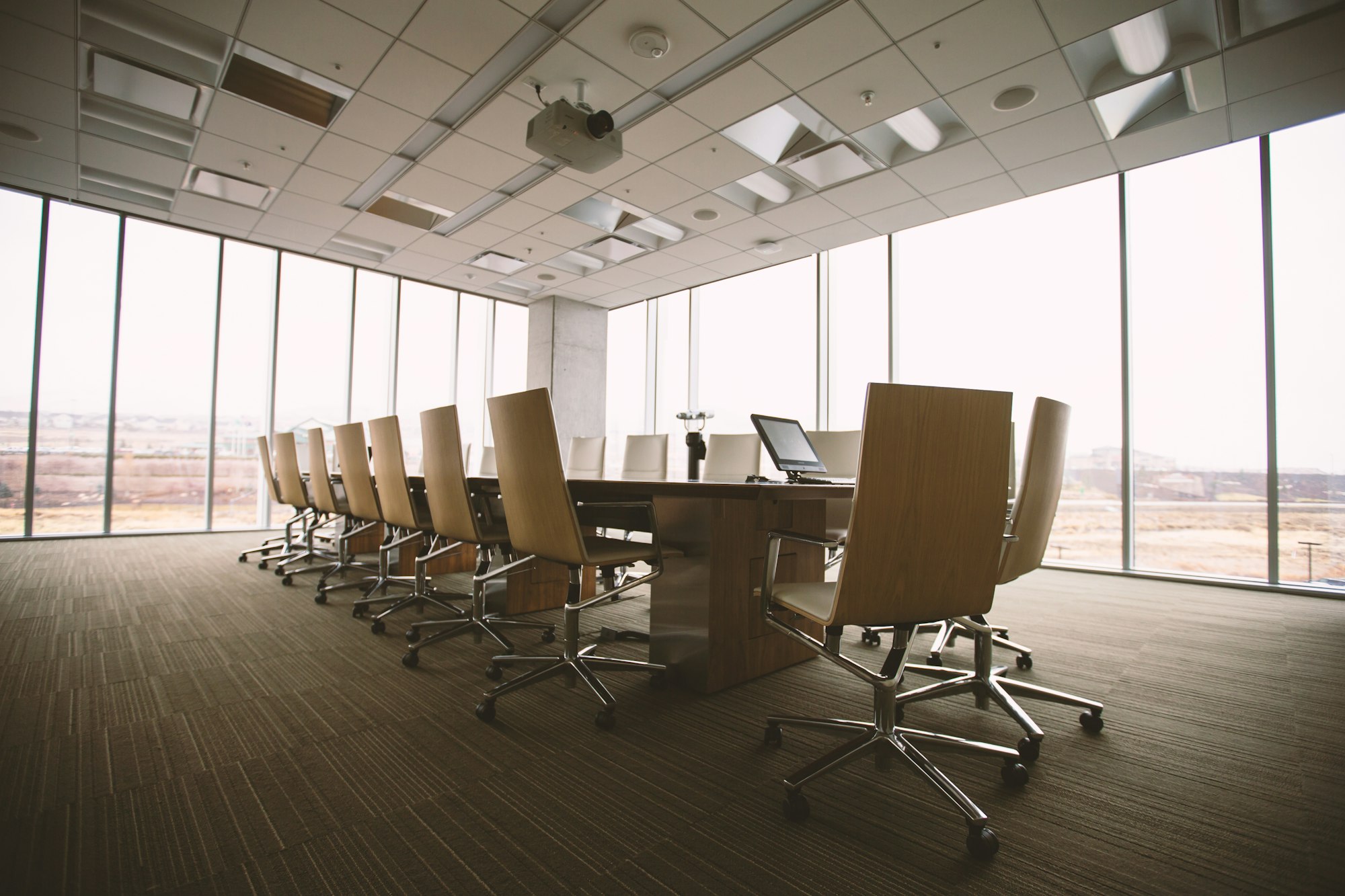 An empty boardroom with a long wooden table, chairs pulled in, and floor-to-ceiling windows.